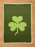 Chunky knit dark green throw blanket with a light green shamrock pattern and cream braided border