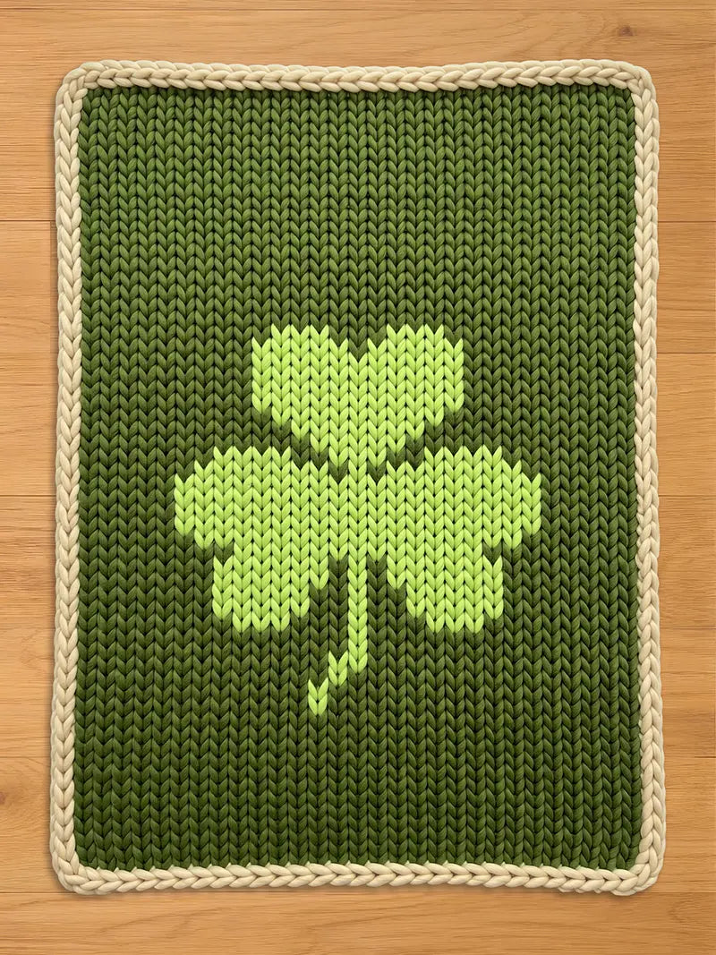 Chunky knit dark green throw blanket with a light green shamrock pattern and cream braided border