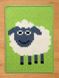 Chunky knit blanket featuring a large, smiling sheep with a white body, blue-grey face, and dark legs, set against a bright green background