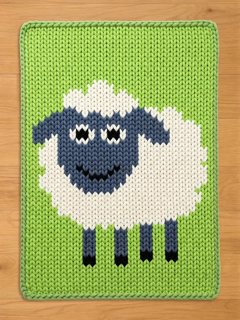 Chunky knit blanket featuring a large, smiling sheep with a white body, blue-grey face, and dark legs, set against a bright green background