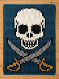 A rectangular knitted textile featuring a central white skull with black eye sockets and nasal cavity, positioned above two crossed grey swords with gold-colored hilts, all set against a solid dark teal blue background.