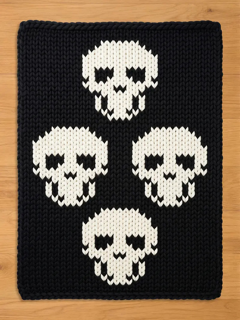 Black chunky knit blanket featuring a bold pattern of four large white skulls arranged in a diamond formation