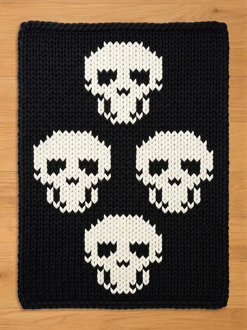 Black chunky knit blanket featuring a bold pattern of four large white skulls arranged in a diamond formation