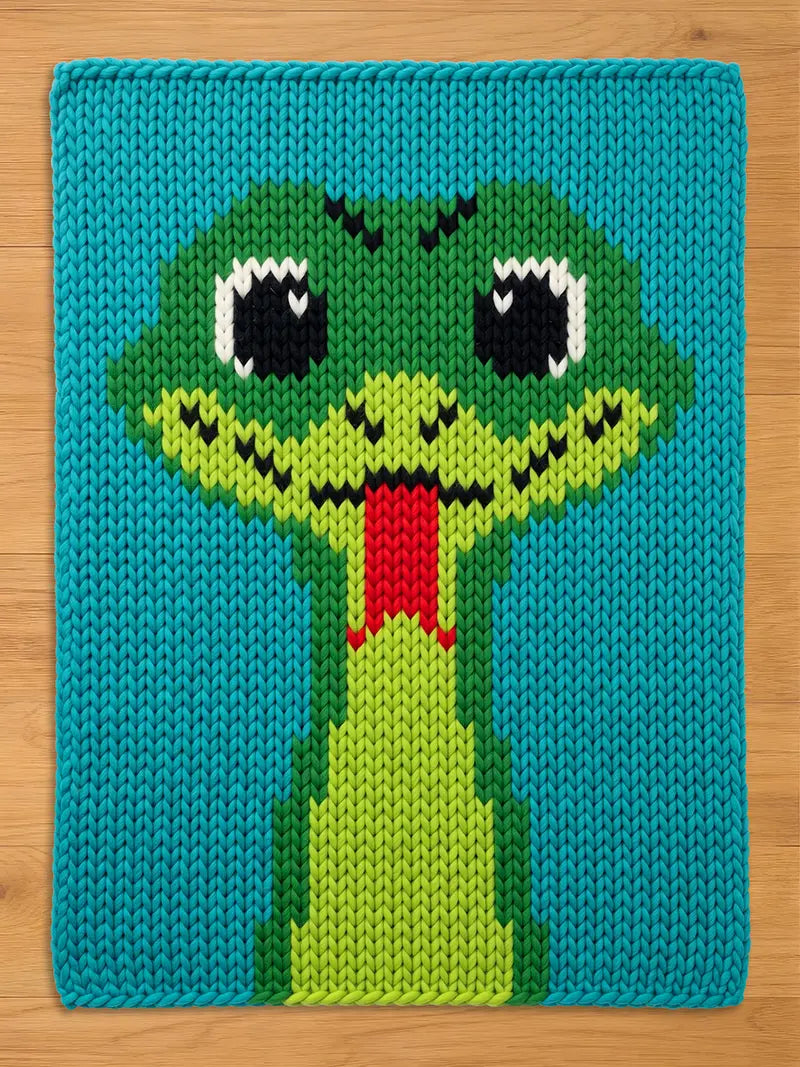 A rectangular knitted blanket featuring a large, centered snake head design. The snake is rendered in shades of lime and forest green with black and white eyes and a bright red forked tongue, all set against a vibrant teal background.