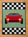 Chunky knit blanket featuring a front-facing red sports car on a light green background, bordered at the top and bottom by black and white racing checkerboard patterns