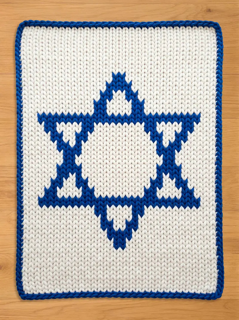 A chunky knitted white and blue Star of David design. The central star is blue, with a white background. The border is blue. The item is likely a decorative piece or a small blanket.
