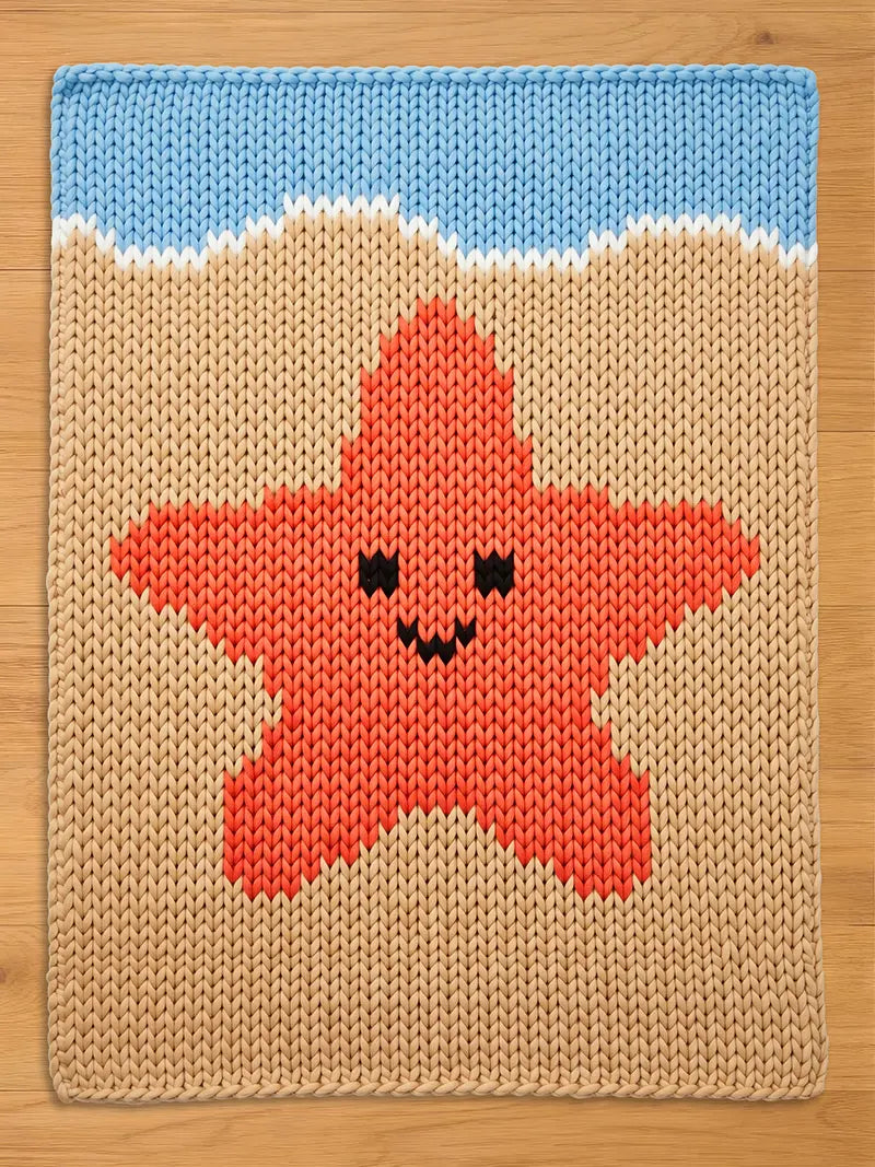 Knitted chunky blanket featuring a smiling orange starfish on a beige background, with a blue sky and white waves at the top. The design is reminiscent of a beach scene, perfect for a child's room or coastal decor.