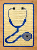 A chunky knit blanket featuring a large blue and grey stethoscope design on a cream background, with a matching blue knitted border