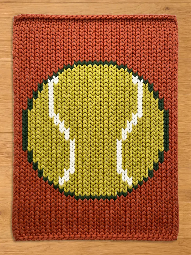Chunky knit blanket featuring a large yellow tennis ball design with white seams, set against a rust orange background