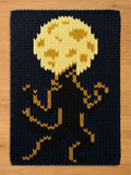 A chunky knit blanket featuring a black silhouette of a werewolf howling at a large, yellow full moon against a dark background