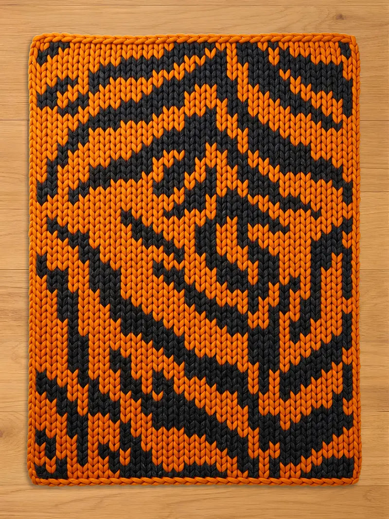 Chunky knit blanket featuring a bold orange and black tiger stripe pattern, laid flat on a light wood surface.