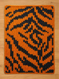 Chunky knit blanket featuring a bold orange and black tiger stripe pattern, laid flat on a light wood surface.