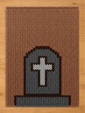 A rectangular knitted chunky blanket featuring a brown background with a centered gray tombstone motif. The tombstone is outlined in dark brown and contains a white cross at its center, with a gray base at the bottom of the design.