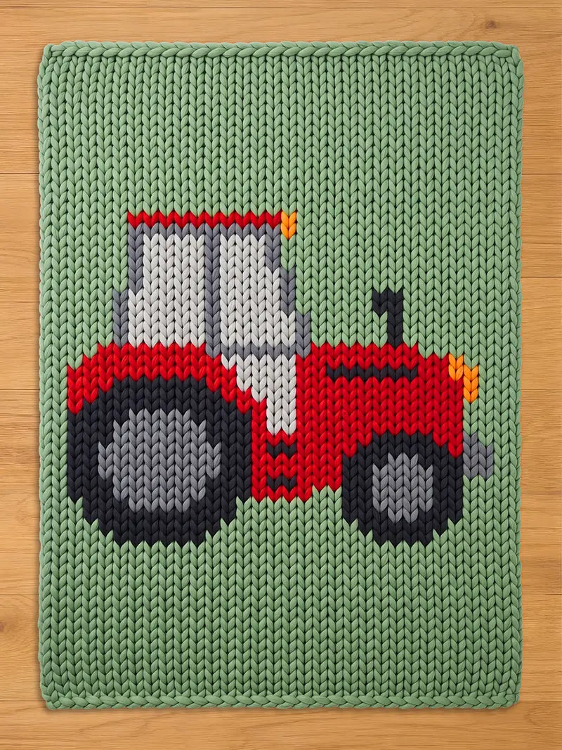 A knitted green blanket featuring a red tractor design. The tractor has gray and black wheels, a white and gray cab, and orange headlights. The blanket is made of a chunky knit material.