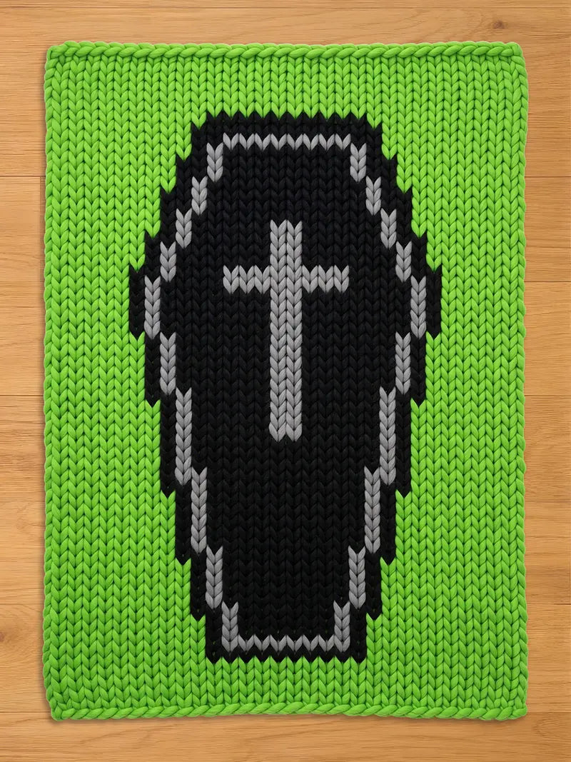 A rectangular knit blanket featuring a bright lime green background with a large, centered black coffin motif. The coffin is outlined in grey and contains a grey cross symbol in the center, all created with a chunky, visible knit texture.