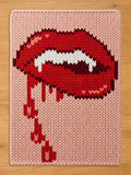A light pink chunky knit blanket featuring a bold graphic of red vampire lips with white fangs and dripping blood