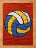 A rectangular knitted blanket featuring a large, centered volleyball graphic. The background is a solid burnt orange, while the volleyball design is composed of thick, textured yarn in vibrant shades of blue, yellow, and white.