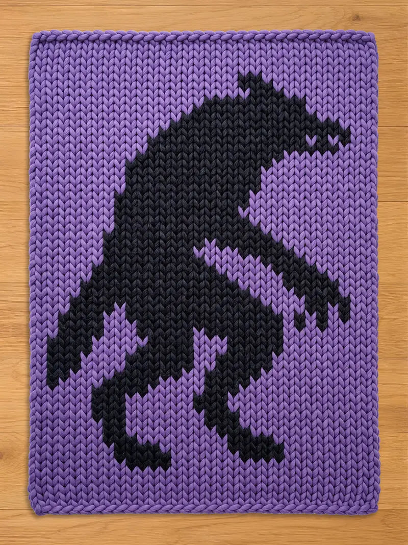 A rectangular chunky knit blanket featuring a large, dark charcoal gray silhouette of a werewolf standing on its hind legs against a vibrant purple background. The thick yarn creates a prominent, textured, and repeating V-stitch pattern.