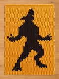 A rectangular knit blanket featuring a bold, black silhouette of a werewolf standing on its hind legs against a vibrant, golden-yellow background. The thick, chunky yarn creates a distinct, textured pattern throughout the entire piece.
