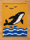 Chunky knit blanket featuring a black and white orca whale breaching over blue waves against a mustard yellow sky