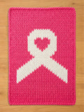 Bright pink chunky knit blanket featuring a large white awareness ribbon design in the center, with a matching pink heart inside the top loop of the ribbon