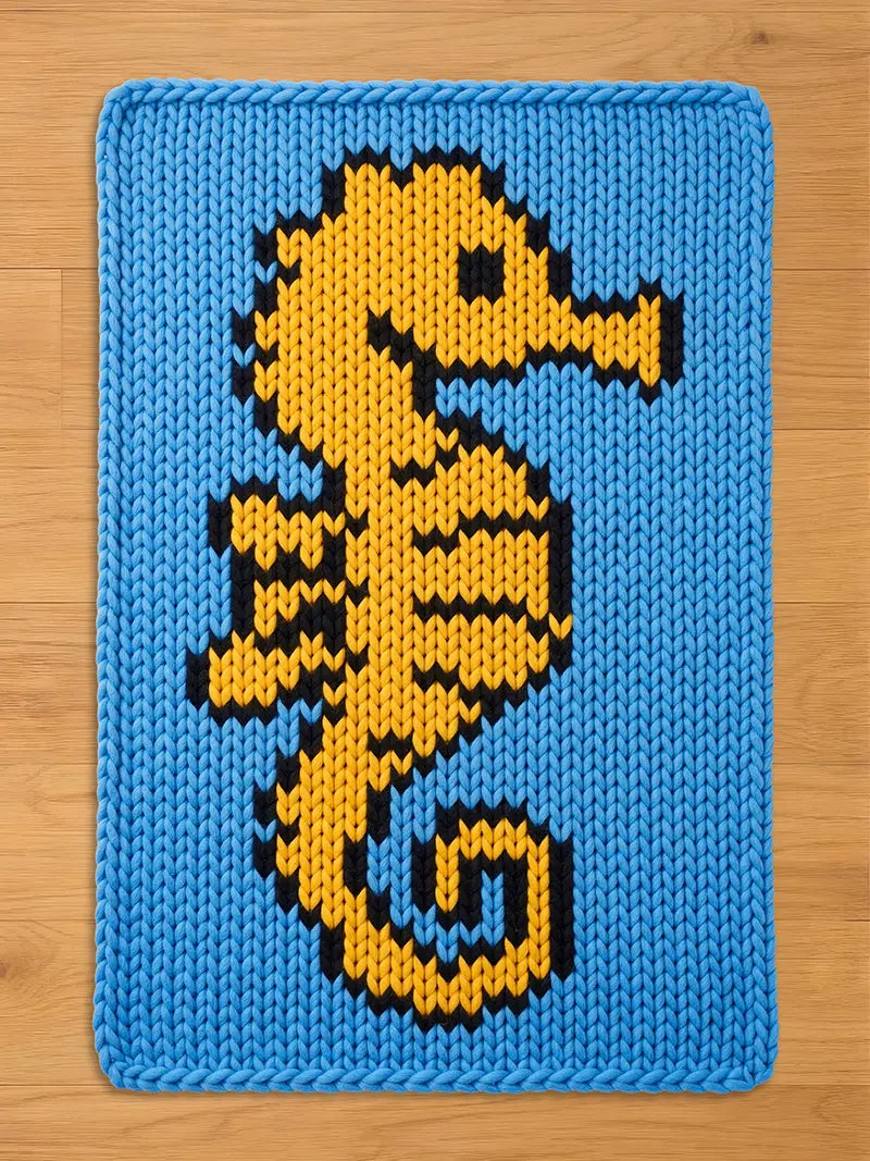 A light blue chunky knit blanket featuring a large yellow seahorse with black accents.