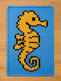 A light blue chunky knit blanket featuring a large yellow seahorse with black accents.
