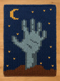 A rectangular knit blanket featuring a dark blue background with a brown earth base at the bottom. A light gray hand emerges from the brown earth. The design includes a yellow crescent moon and small yellow stars scattered throughout.